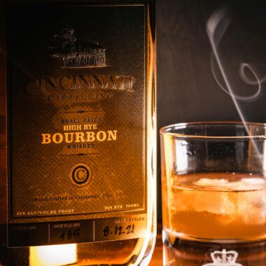 A close-up of a Cincinnati Distilling Bourbon bottle and glass with ice.