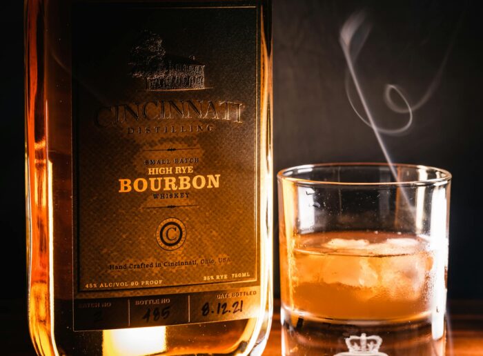 A close-up of a Cincinnati Distilling Bourbon bottle and glass with ice.