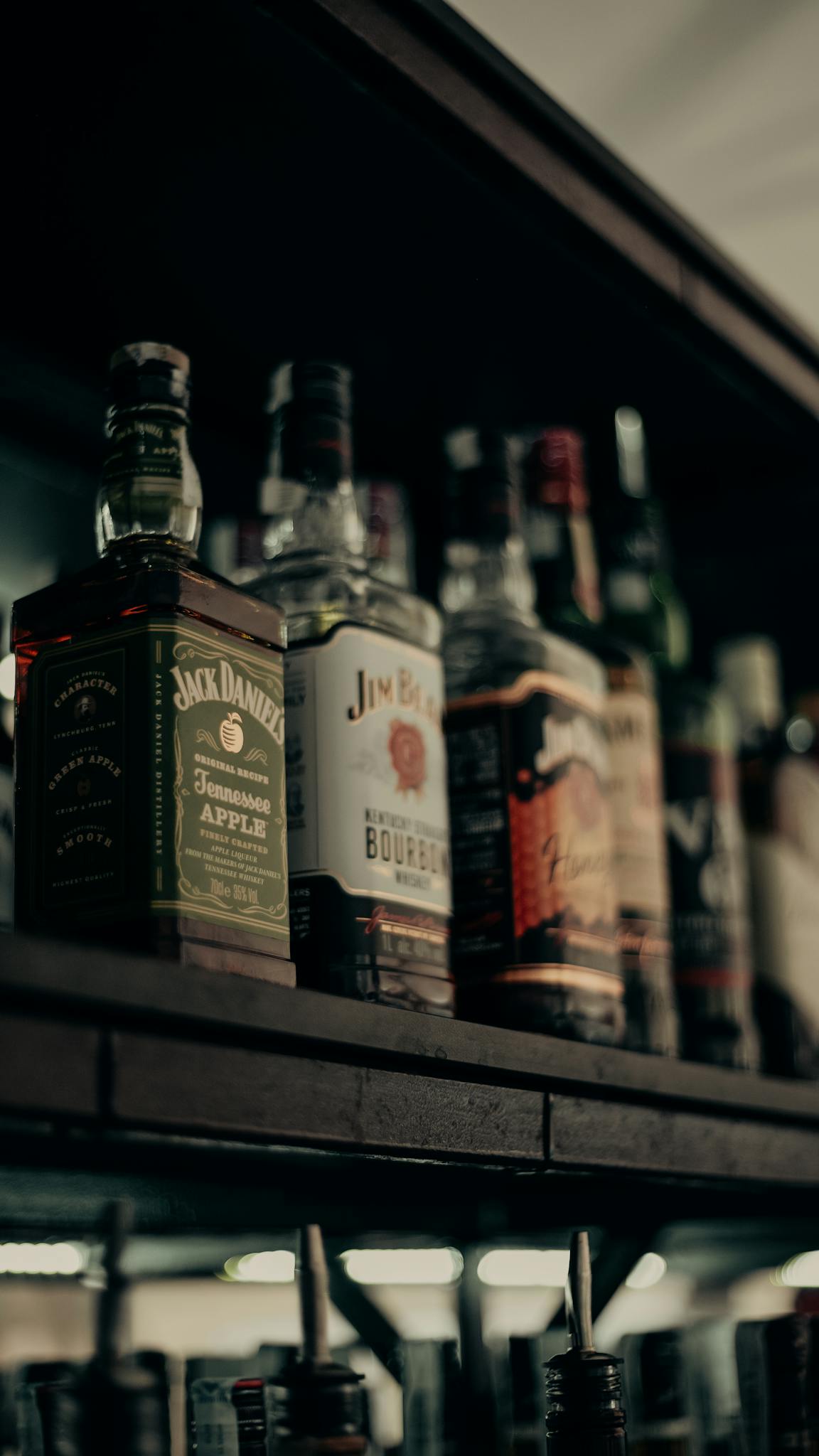 Aesthetic close-up shot of various whiskey bottles arranged neatly on a bar shelf.