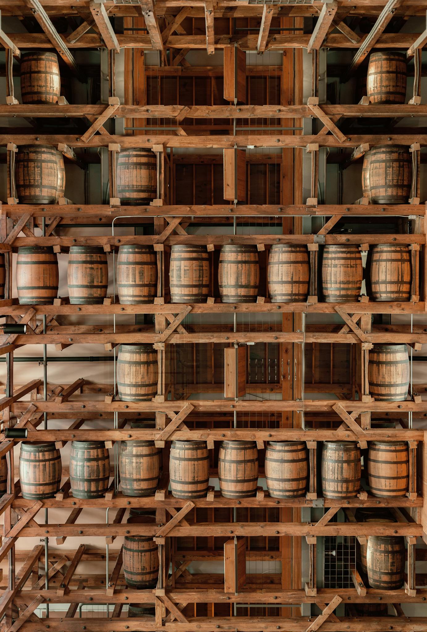 Vertical view of wooden barrels in a distillery storage with wooden shelves.